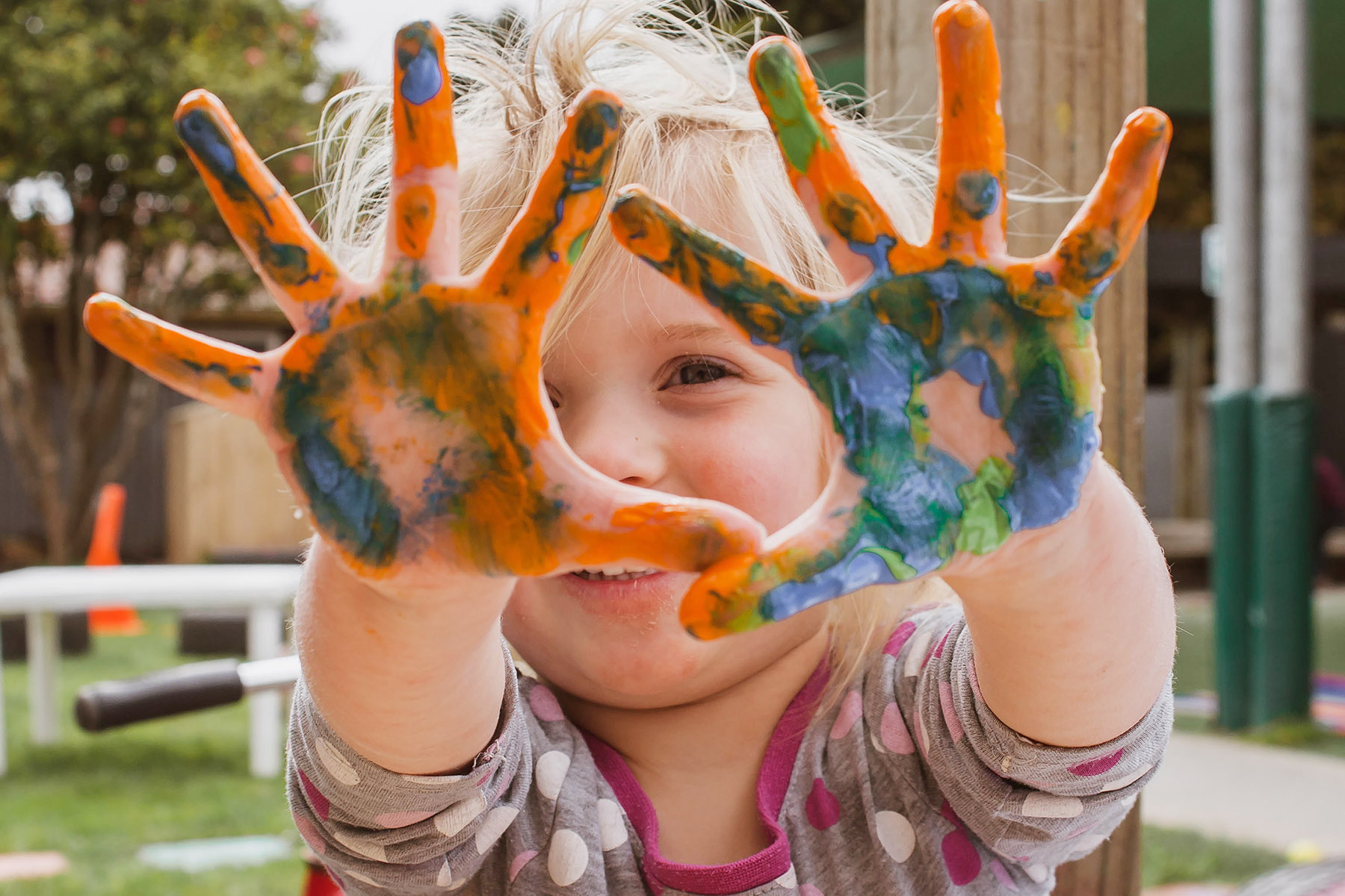 Ein lächelndes kleines Mädchen zeigt stolz seine bunten Hände, die mit Fingerfarbe bepinselt wurden.