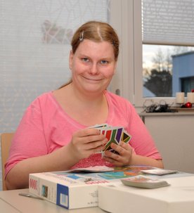 Eine lächelnde Frau sitzt an einem Tisch und sortiert ein Kartenspiel.