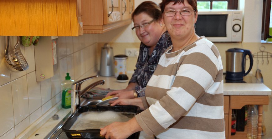 Zwei Frauen stehen lächelnd in einer Küche und machen den Abwasch.
