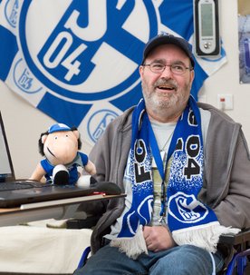 Ein großer Schalke 04 Fußballfan sitzt lachend in seinem Rollstuhl.