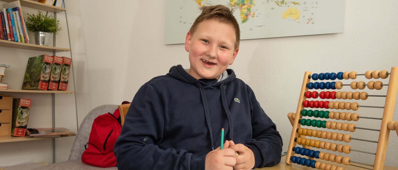 Ein lächelnder Junge sitzt in seinem Kinderzimmer an seinen Mathematik-Hausaufgaben. TG_Fuhlenbrock.JPG