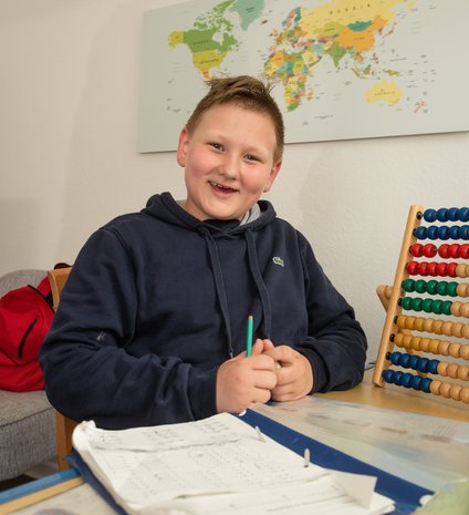 Ein lächelnder Junge sitzt in seinem Kinderzimmer an seinen Mathematik-Hausaufgaben.