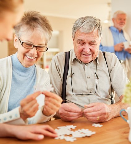 Zwei lächelnde Senioren spielen ein Pussel.