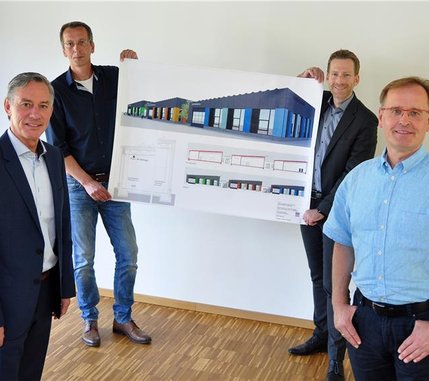 Vier Männer präsentieren stolz ein Plakat. Das Plakat kündigt den Neubau der Rheinbabenwerkstatt an.