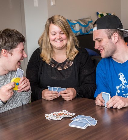 Drei junge Erwachsene sitzen an einem Tisch und spielen gut gelaunt Karten.